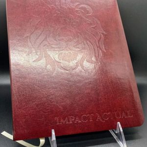 Burgundy leather journal with an embossed lion head design and “Impact Actual” text on the cover.